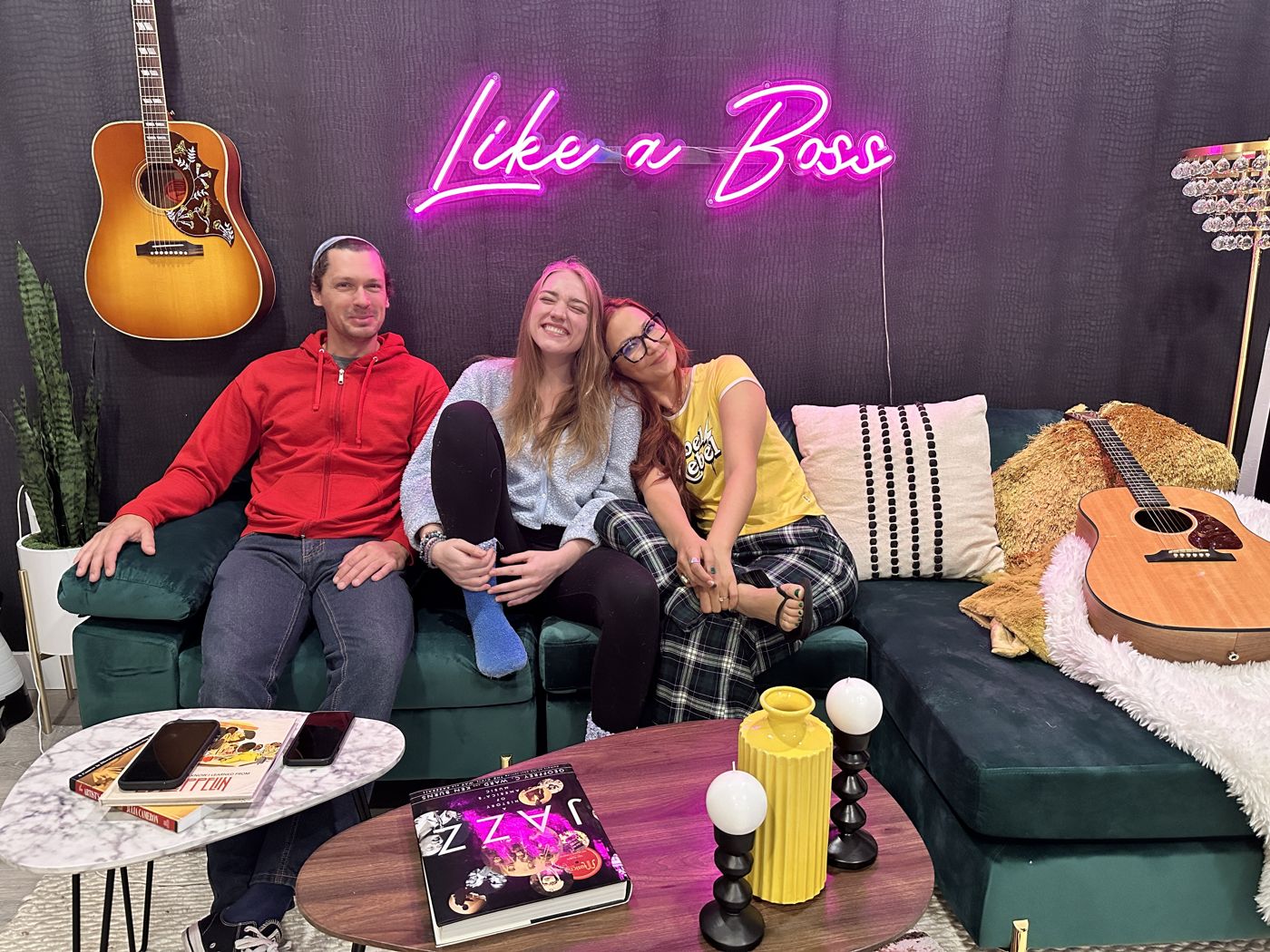 Kris Bradley with co-writers Justin Merrill and Stelle Amor on a green couch under a pink Like a Boss neon sign